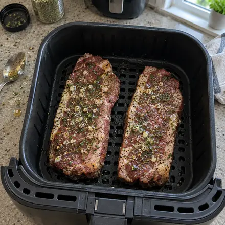 Zwei gewürzte, rohe Steaks nebeneinander im Airfryer-Korb